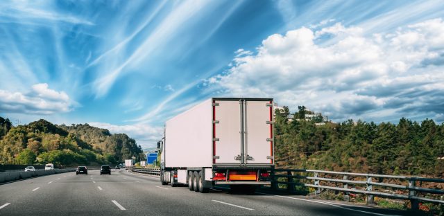 Truck Or Traction Unit In Motion On Road, Freeway. Asphalt Motorway Highway Against Background Of Forest Landscape. Business Transportation And Trucking Industry